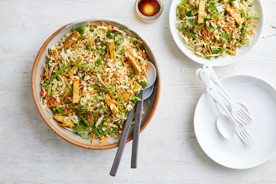Two plates of colorful Asian salad with chopsticks and forks on a wooden table.