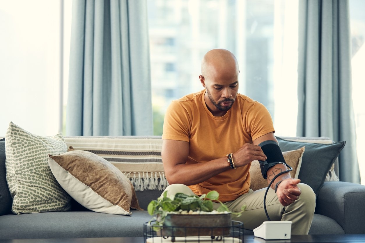 A man sitting on a couch, using a blood pressure monitor to measure his blood pressure levels.