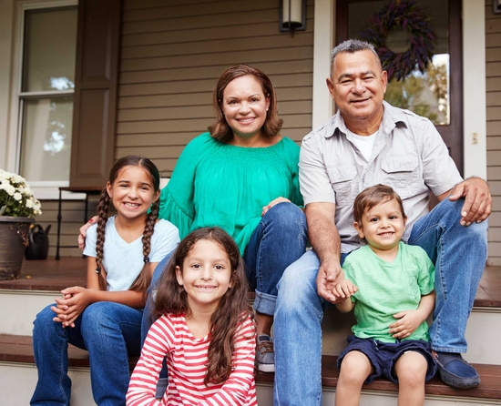 Family of five (male & female parents and three kids) sitting on steps of their house, smiling