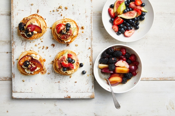 Four short stack of pancakes with two bowls of fruits, berries and nuts