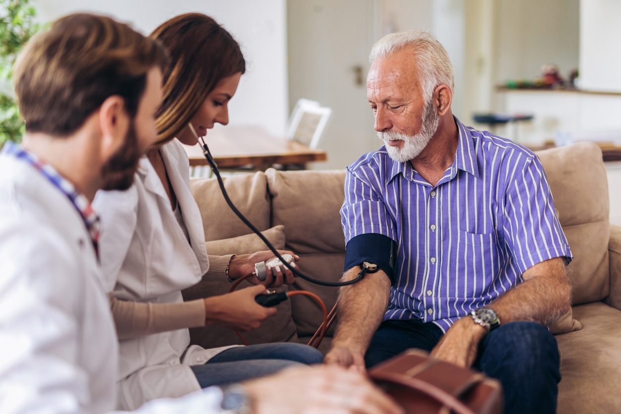 Mature man having blood pressure checked by two health professionasl