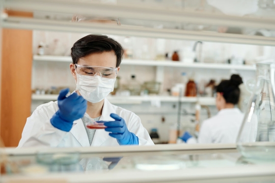 A scientist in a lab coat and gloves carefully holds a test tube, conducting an experiment.