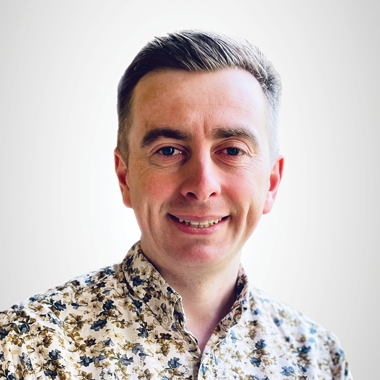 Peter Thomas wearing a floral shirt smiles warmly 