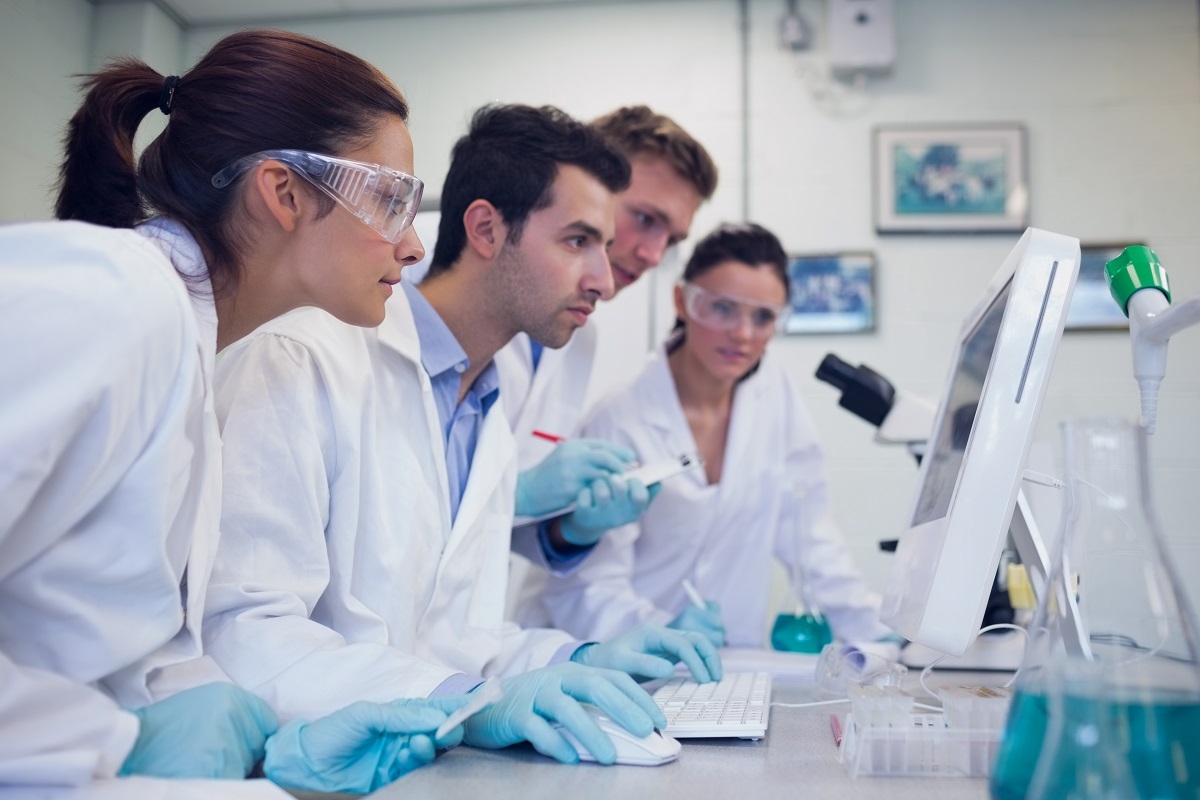 A group of scientists in lab coats observing a computer screen in a research laboratory.